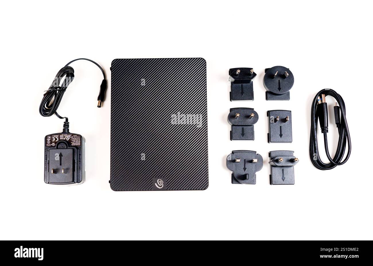 Kiev, Ucraina - 23 ottobre 2024: Disco rigido Seagate portatile accompagnato da un adattatore di alimentazione e da più adattatori di spina globali disposti su un supporto bianco Foto Stock
