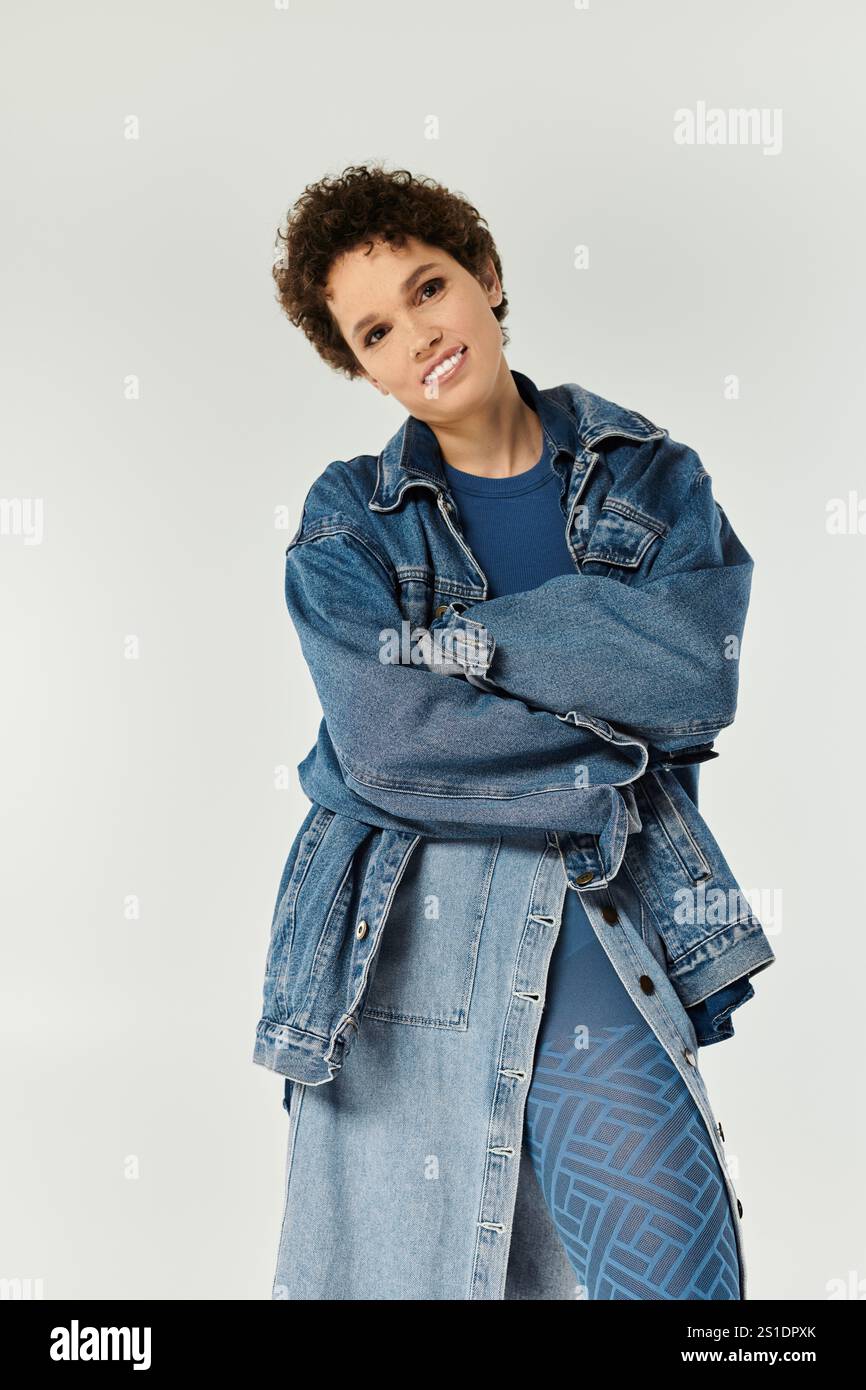 Una giovane donna elegante trasuda fiducia nei denim alla moda mentre si posa su uno sfondo neutro. Foto Stock