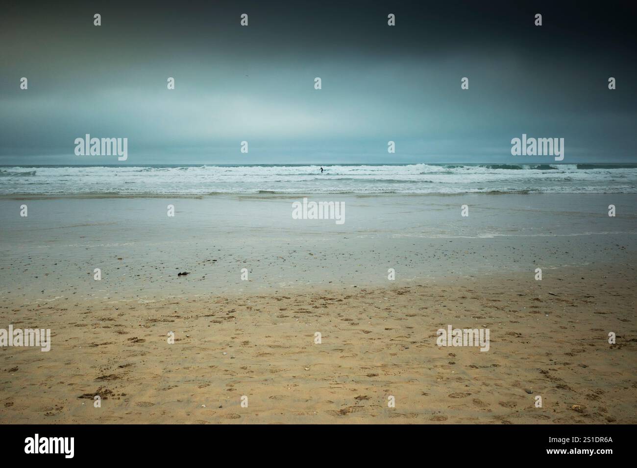 La figura di un surfista solitario che cavalca un'onda a Fistral Beach in un giorno di Natale freddo e nebbioso a Newquay, in Cornovaglia, nel Regno Unito. Foto Stock