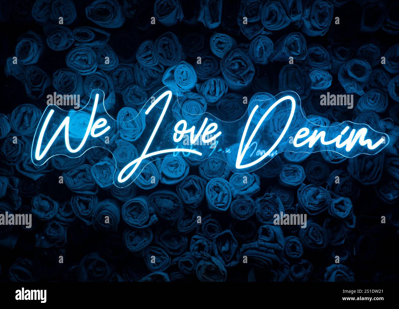 Insegna blu al neon "We Love Denim" davanti allo sfondo dei jeans. Foto Stock
