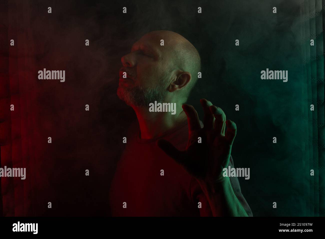 ritratto di uomo bianco, calvo e barbuto, che esprime la fotocamera. Isolato su sfondo nero fumé con luci colorate. Pers. Sudamericano Foto Stock