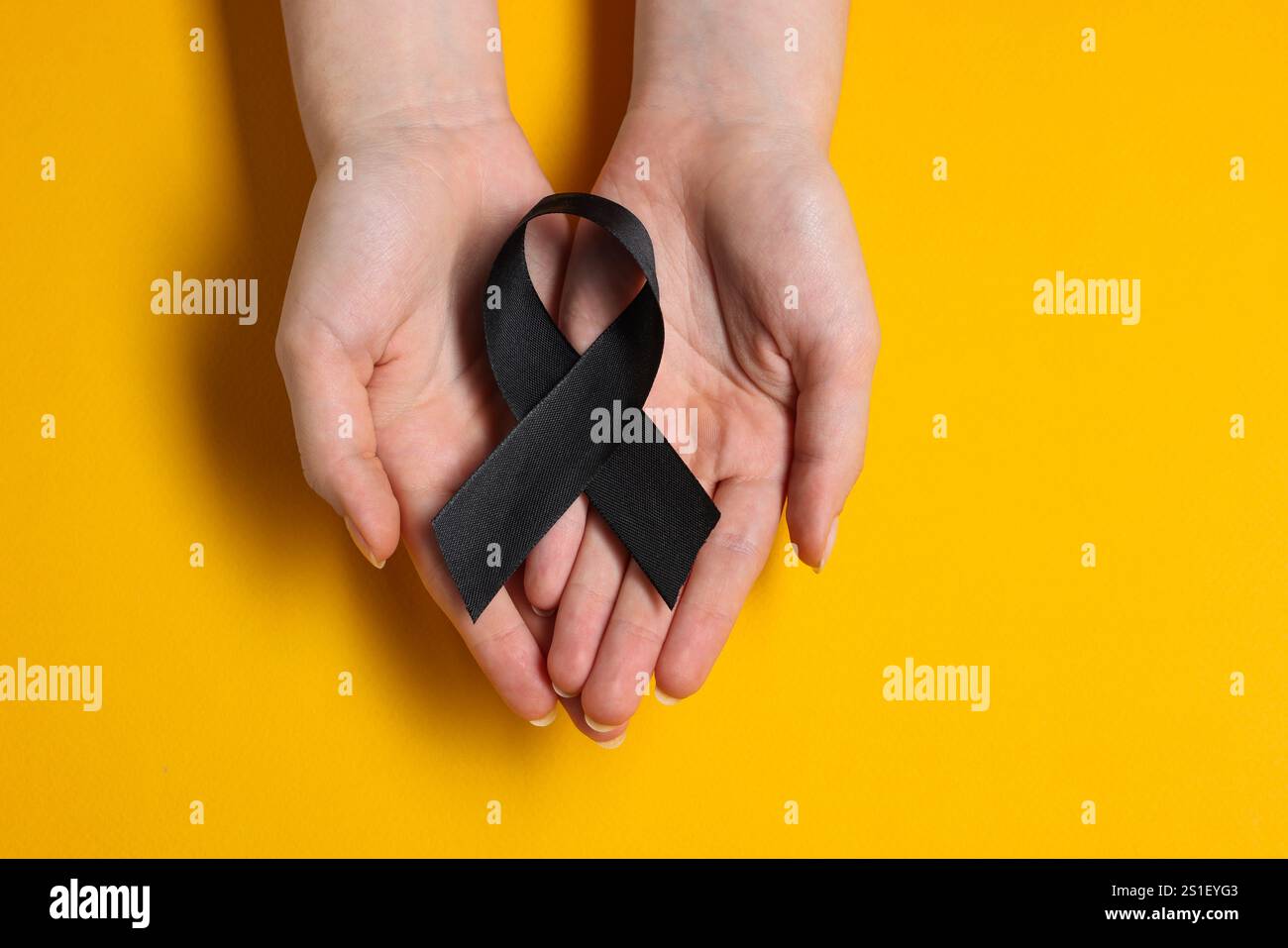 Donna con nastro nero su sfondo giallo, vista dall'alto. Concetto di melanoma e lutto Foto Stock