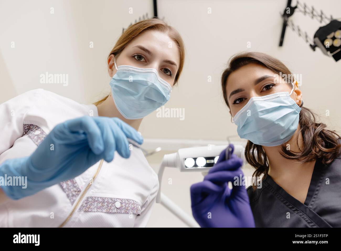 Dal basso dentisti con specchio e dispositivo piegato sopra la paziente durante l'appuntamento in clinica odontoiatrica. Foto Stock