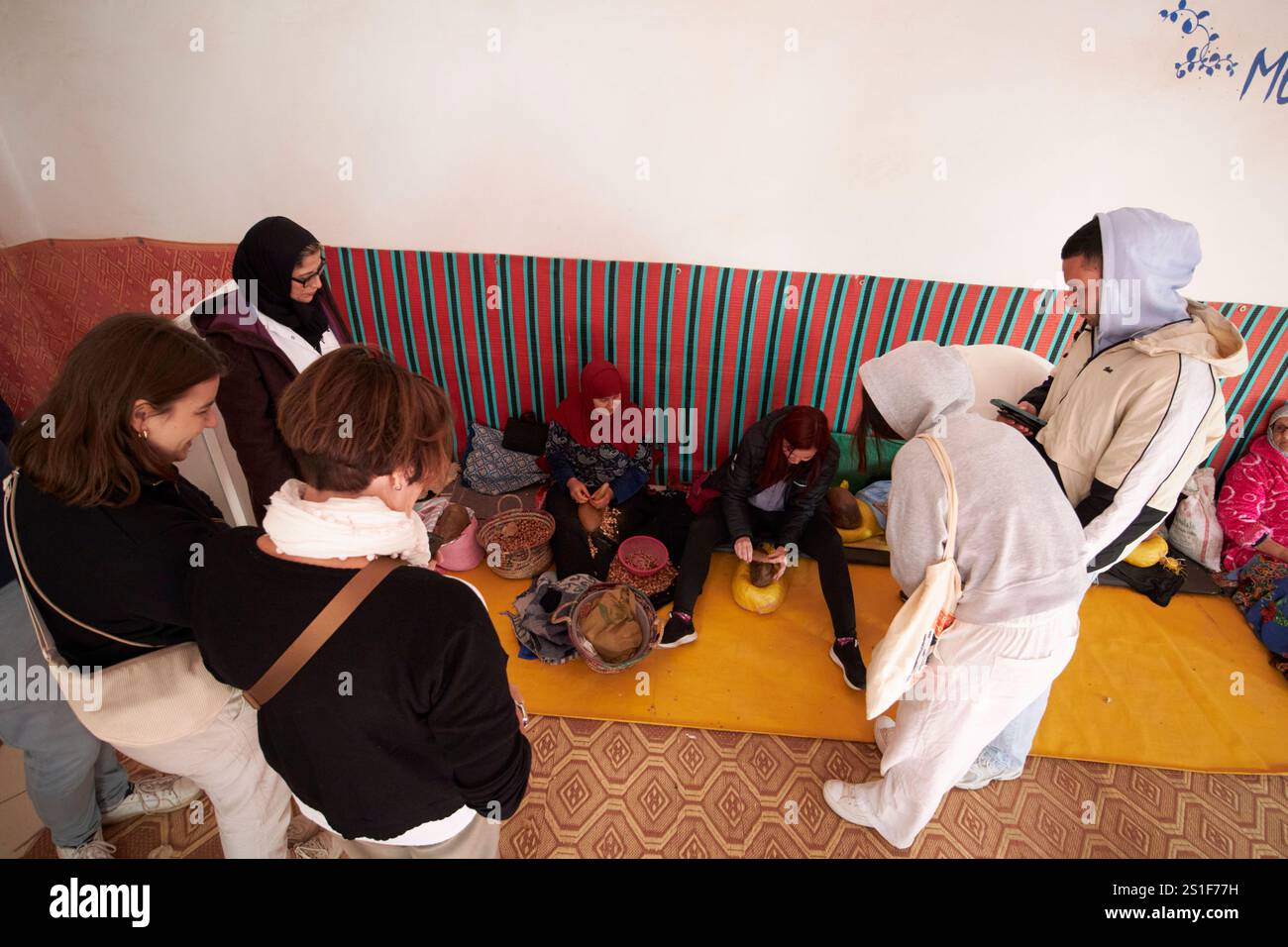 turisti che aiutano una donna a bombardare le noci di argan durante una visita a un collettivo di donne del petrolio di argan in marocco Foto Stock