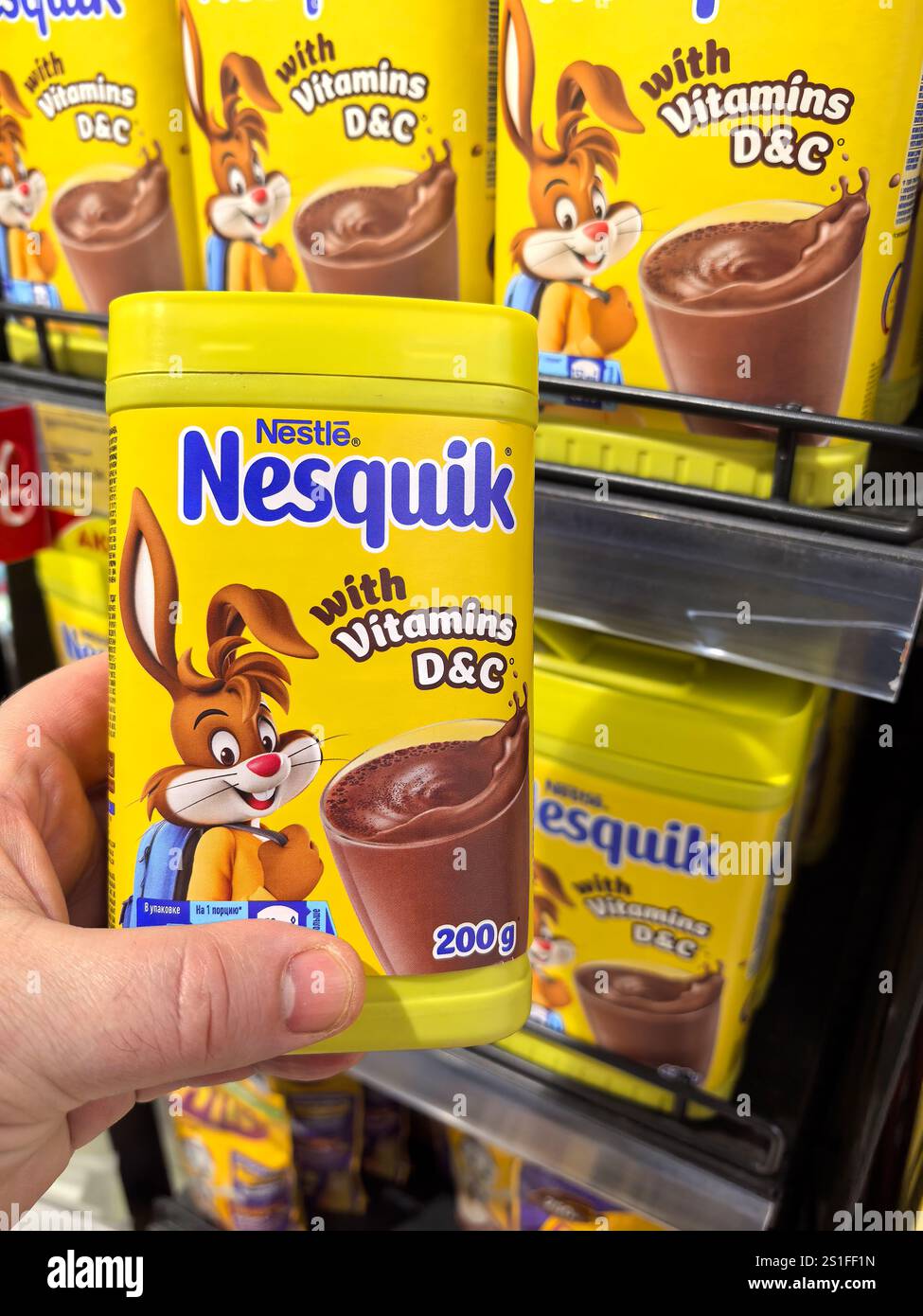 Bobruisk, Bielorussia - 29 dicembre 2024: Una persona tiene in mano un contenitore giallo brillante di miscela di cioccolato con un coniglio giocoso in un negozio di alimentari ben fornito Foto Stock