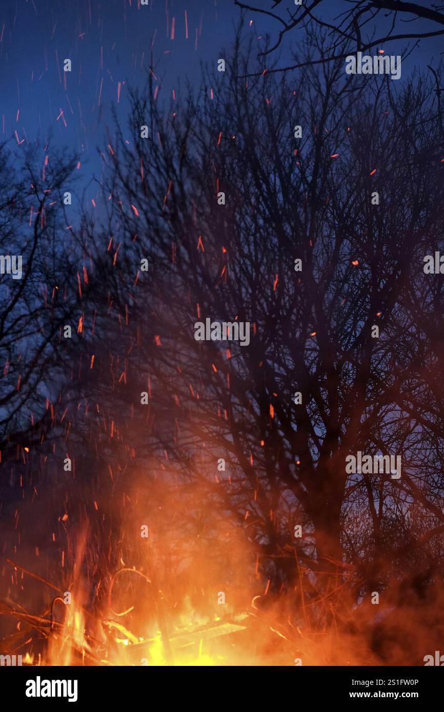 Fiamme scoppiettanti con scintille volanti si tuffano nel cielo blu scuro della sera. Formato verticale. Le fiamme scoppiettanti con scintille volanti si infrangono nel blu scuro Foto Stock