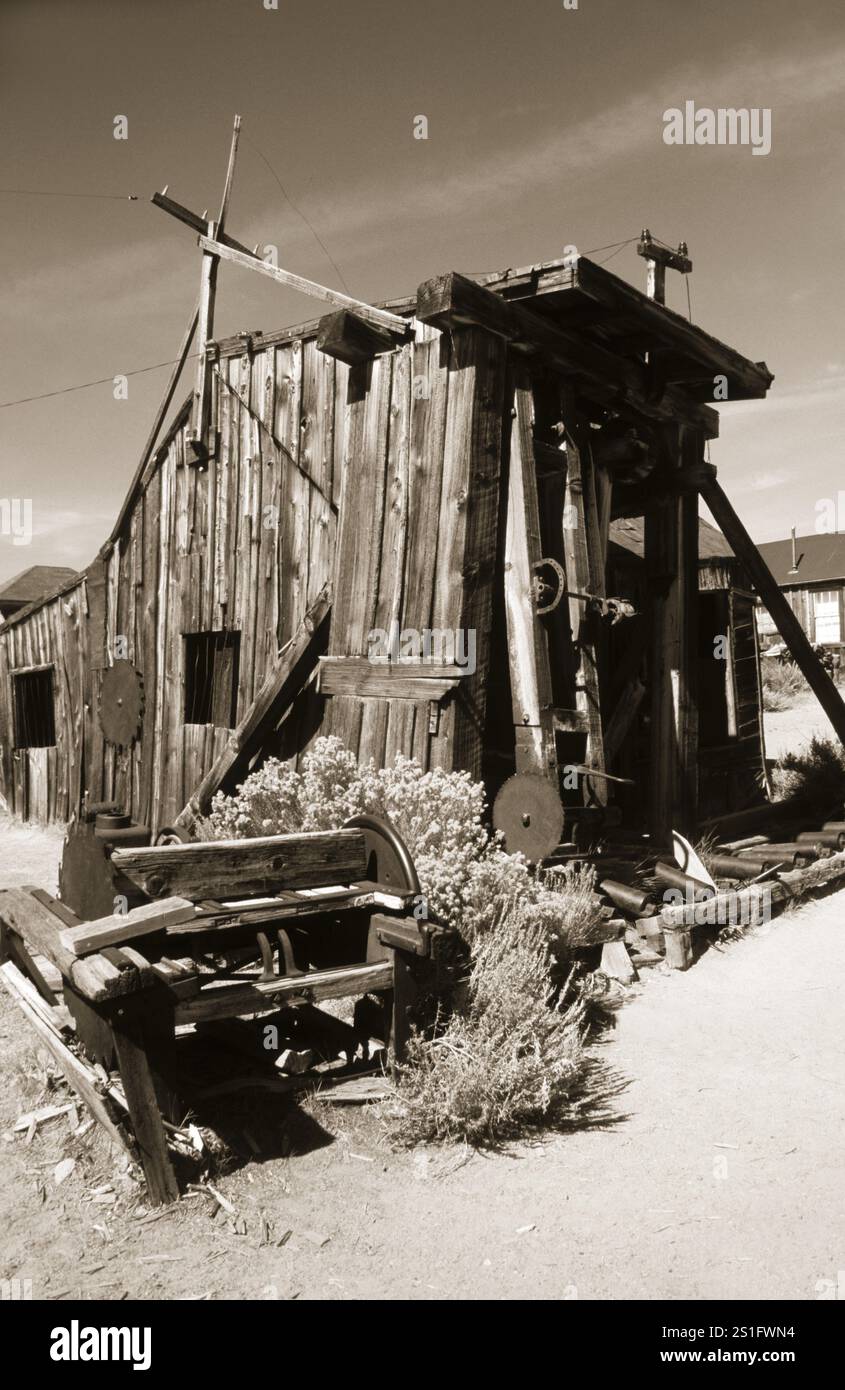 Capannone in legno deformato e deformato con attrezzature tecniche di fronte ad esso, nell'ex città mineraria dell'oro di Bodie. Foto in tonalità seppia. Attrezzatura tecnica Foto Stock