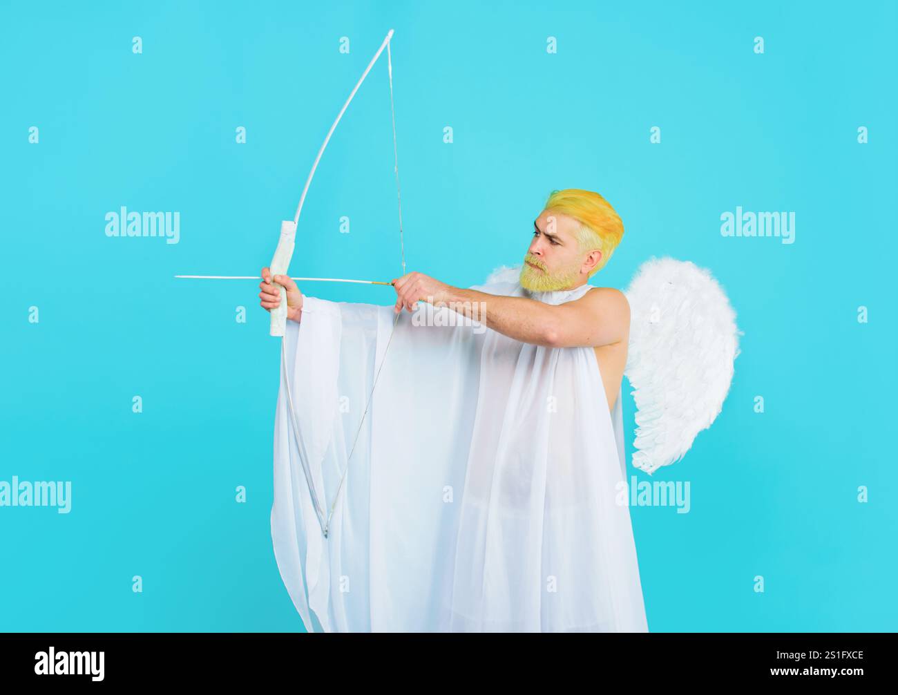 Festa di San Valentino. Uomo barbuto con ali d'angelo che spara freccia d'amore da prua. Dio dell'amore. Bel cucciolo maschile in costume da angelo con arco Foto Stock