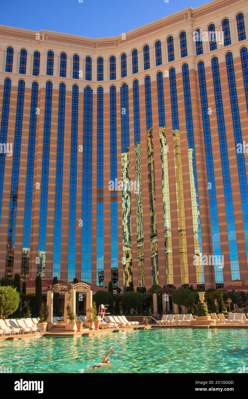 Un grande hotel con una piscina e un uomo che ci sta nuotando. La piscina è circondata da alberi e l'hotel è molto alto Foto Stock