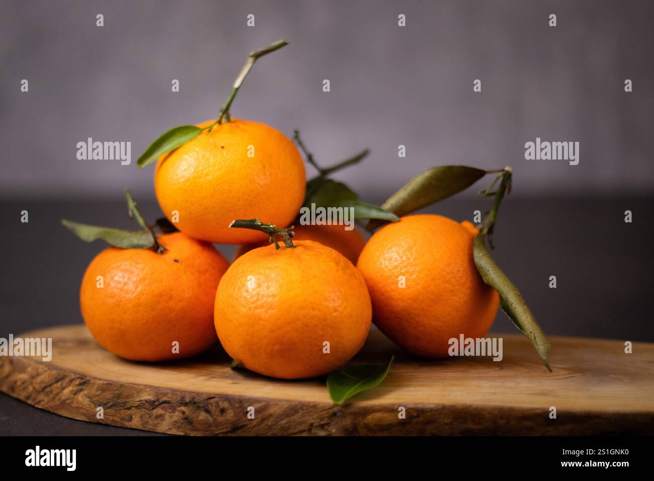 Un mucchio di frutti mandarini interi con foglie su piatto di legno, sfondo grigio del tavolo Foto Stock