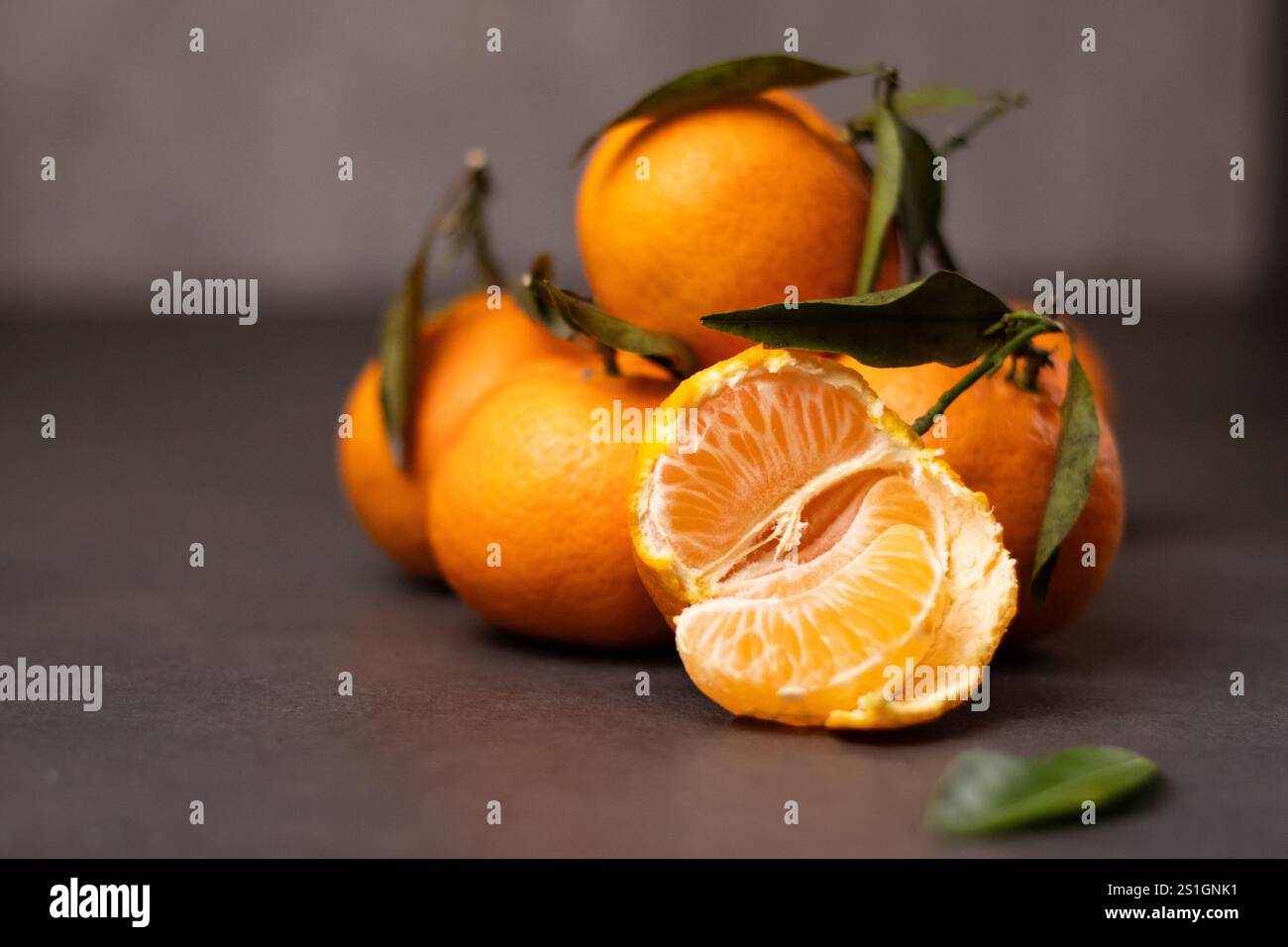 Un mandarino sbucciato e un mandarino intero con foglie su sfondo grigio Foto Stock