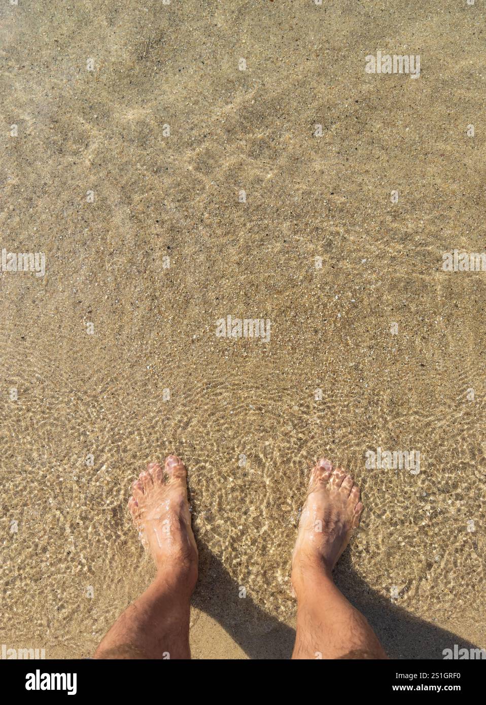 Gambe da uomo in acqua limpida. Fondo sabbioso con bagliore del sole, mare cristallino, sensazione di relax. Concetto di vacanza e vacanza. Foto Stock