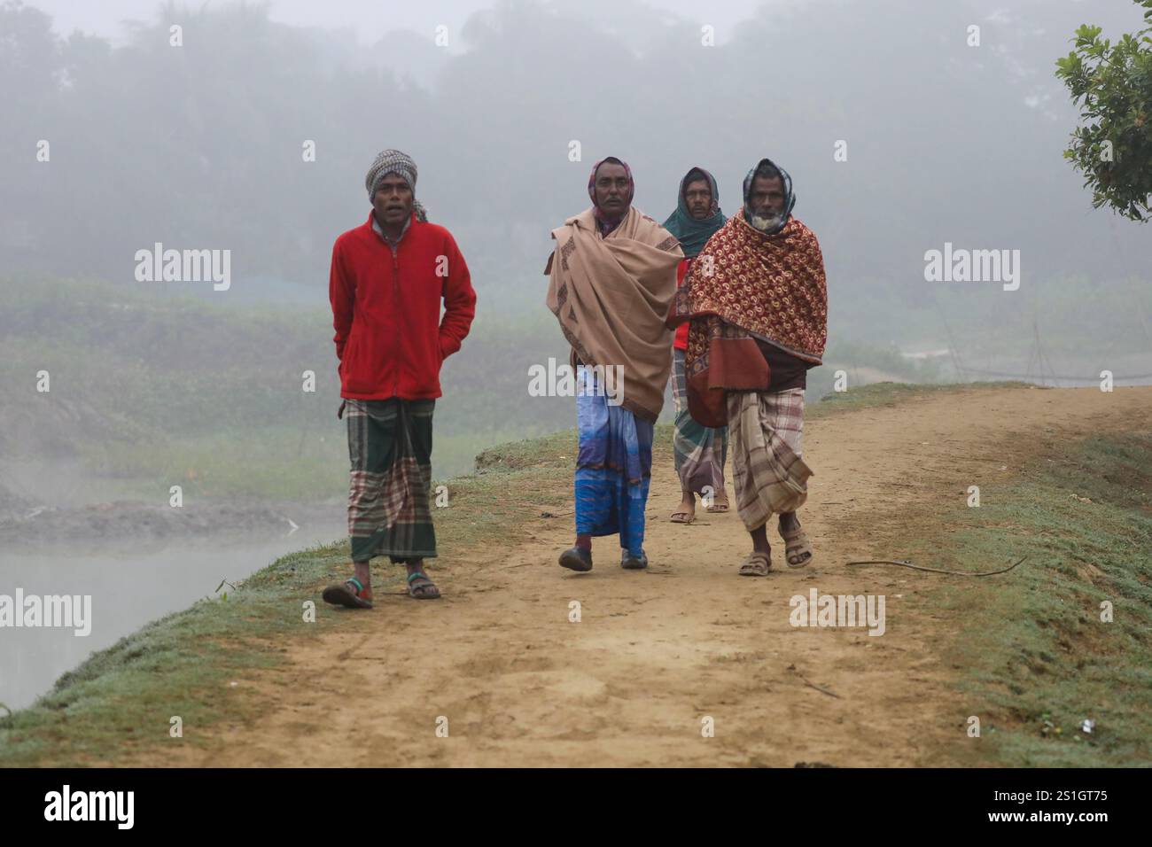 Un gruppo di anziani che camminano attraverso una strada fangosa nella zona di Haor di Mohonganj, distretto di Netrokona, Bangladesh, in una nebbiosa mattina invernale. Foto Stock