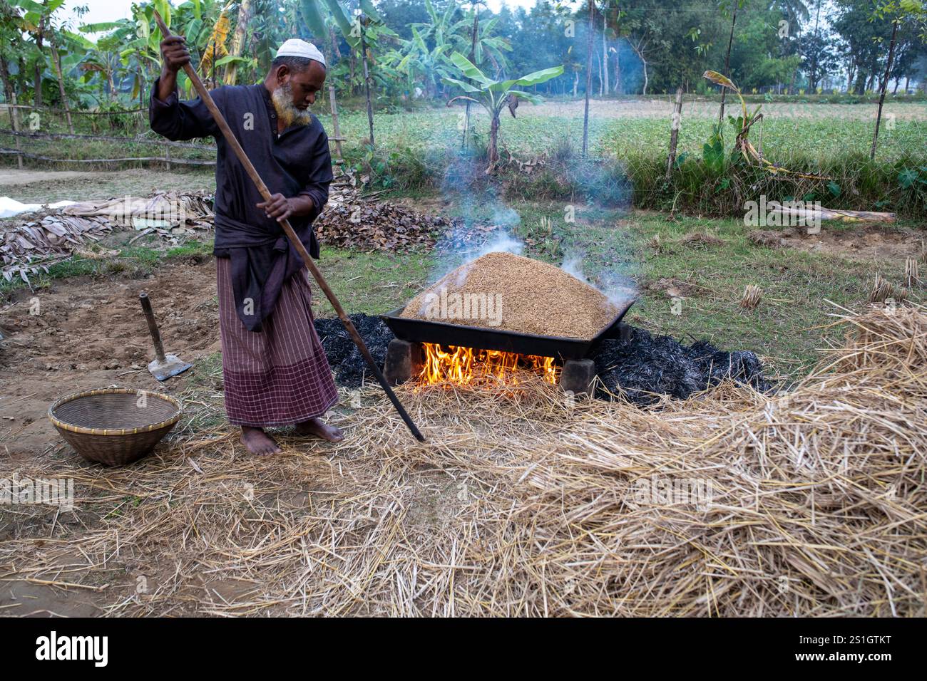Un agricoltore fa bollire il risone nella regione Haor di Mohonganj, distretto di Netrokona, Bangladesh, durante la stagione del raccolto. Foto Stock