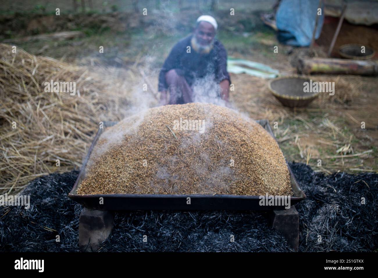 Un agricoltore fa bollire il risone nella regione Haor di Mohonganj, distretto di Netrokona, Bangladesh, durante la stagione del raccolto. Foto Stock