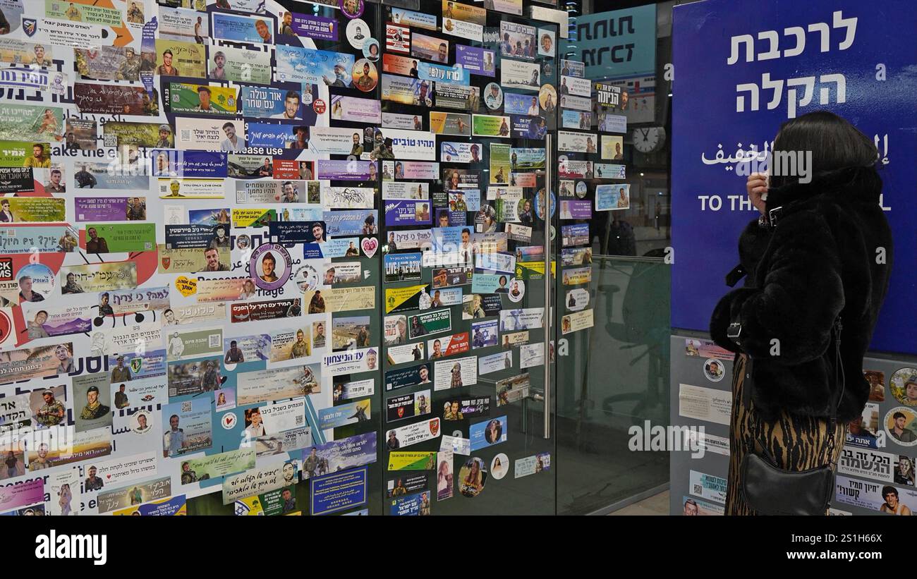 Una donna israeliana guarda un muro con adesivi commemorativi che commemorano i soldati IDF e i civili uccisi nella guerra israeliana a Gaza e ter­ror vic­tims dopo Octo­ber 7, nella stazione ferroviaria di Savidor, nel mezzo delle continue battaglie tra Israele e il gruppo militante Hamas a Gaza il 2 gennaio 2025 a Tel Aviv. Israele. Foto Stock
