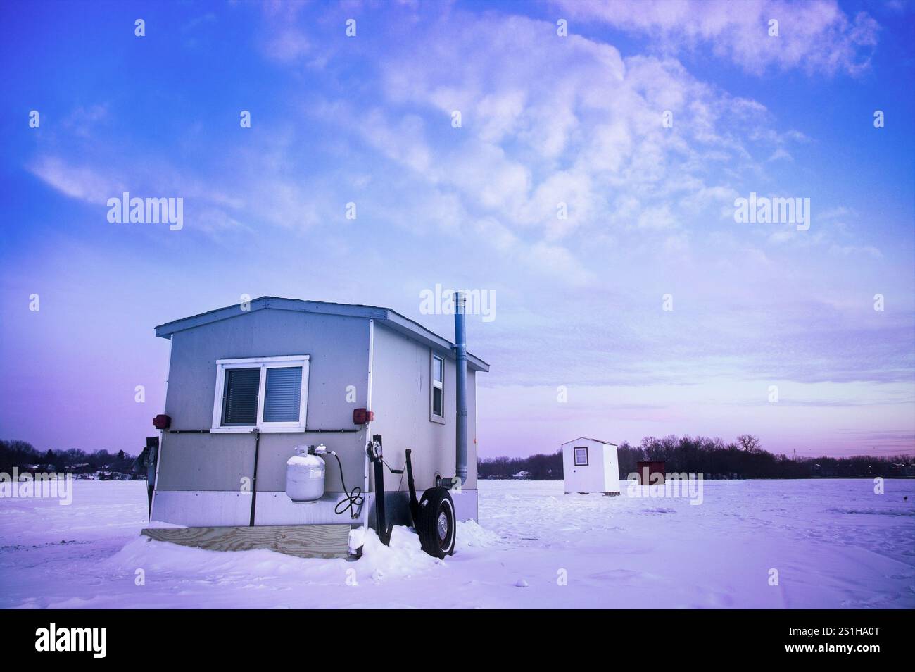 Un'accogliente baracca per la pesca sul ghiaccio si trova in cima alla distesa ghiacciata del lago Medicine vicino a Minneapolis, Minnesota, circondato da un vasto paesaggio innevato. Foto Stock