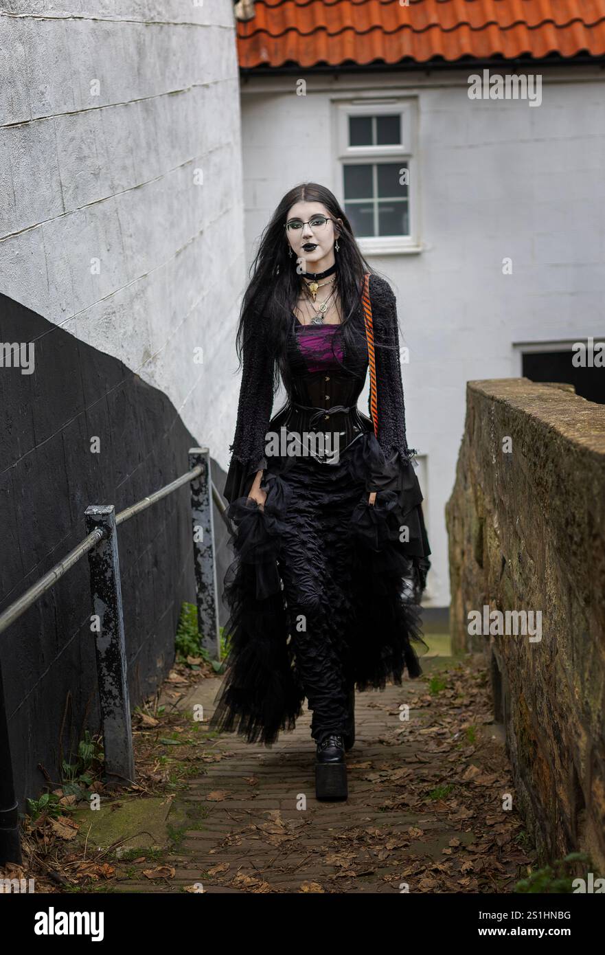 Una ragazza gotica sottile che cammina su un sentiero acciottolato a whitby, nel nord dello yorkshire Foto Stock