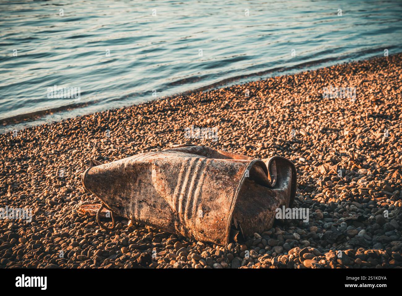Botte di stagno arrugginito sulla riva ghiaia di un fiume Foto Stock