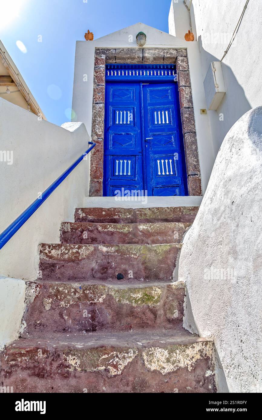 Porta in legno blu brillante su gradini in pietra rustica alla luce del sole del Mediterraneo, Oia, Santorini, Grecia Foto Stock