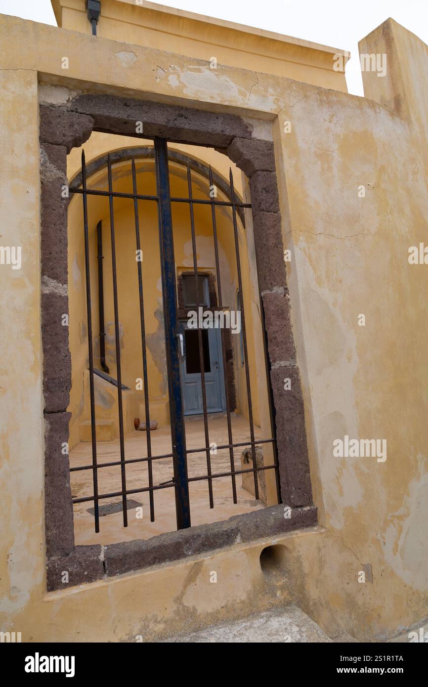Porta in ferro battuto che conduce a un vecchio edificio con un muro giallo testurizzato, Santorini, Grecia Foto Stock