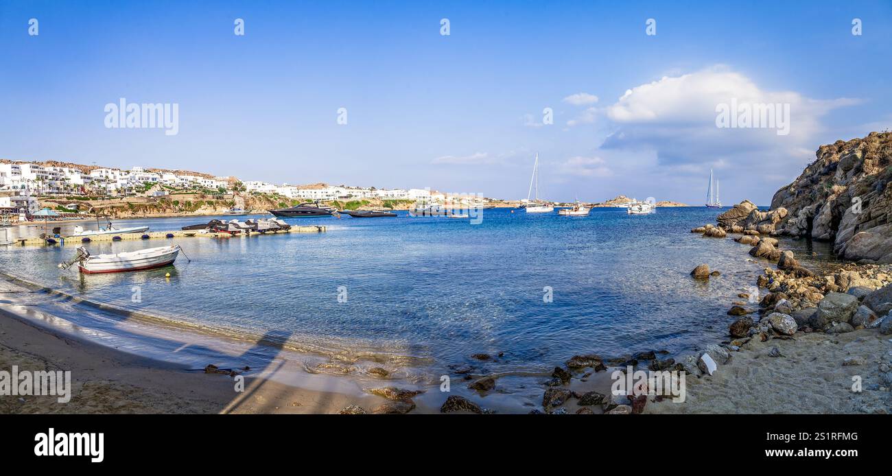Villaggio costiero con barche sulla panoramica baia mediterranea sotto i vibranti cieli blu, Mykonos, Grecia Foto Stock