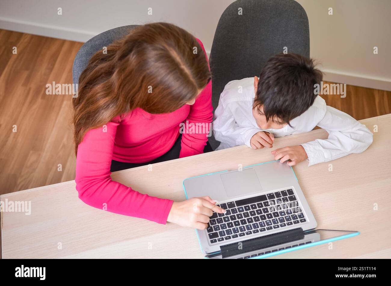 Babysitter che punta alla tastiera del notebook, aiuta un bambino con i compiti, visto dall'alto Foto Stock