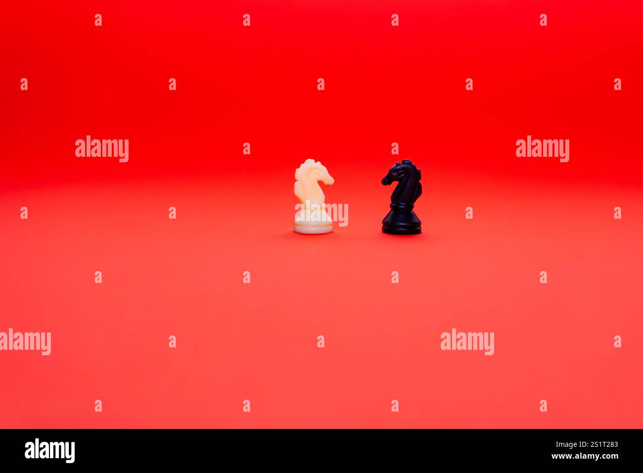 Due cavalieri degli scacchi, uno bianco e uno nero, si stagliano su uno sfondo rosso vivo, simboleggiando un'intensa battaglia strategica tra le forze avversarie in t Foto Stock