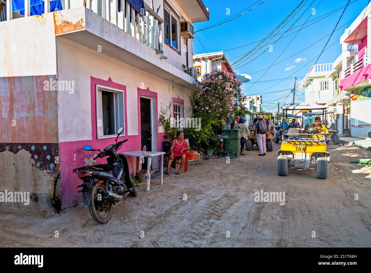 Vivace scenario di Village Street con persone e trasporto sotto un cielo limpido, Isla Holbox, Messico Foto Stock