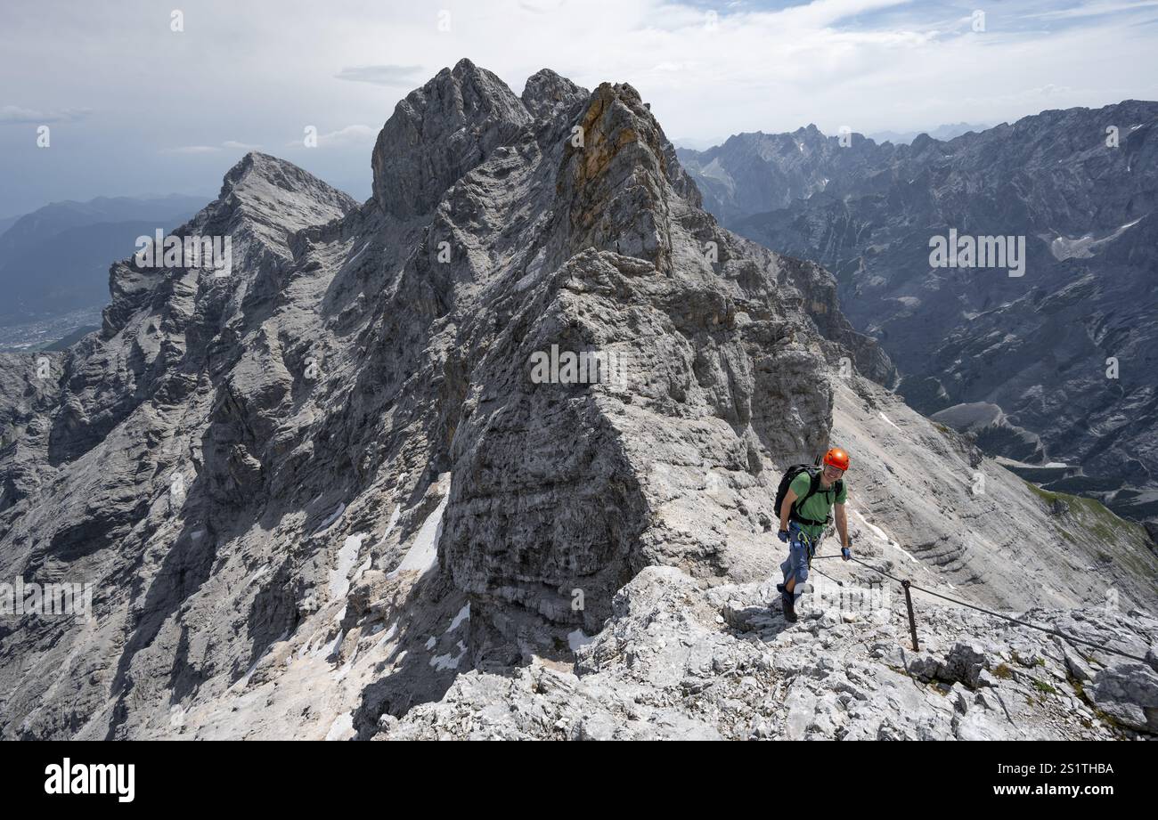 Alpinista con casco che sale in una salita sicura sulla roccia, su una stretta cresta rocciosa, attraversando il Jubilaeumsgrat, vista del Rheintal e dell'Alpspitze Foto Stock