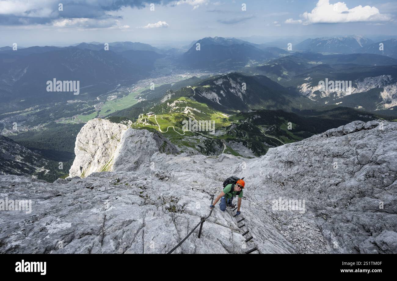 Alpinista con casco che sale sulla roccia in una salita sicura, su una stretta cresta rocciosa, in ripido paesaggio roccioso di montagna, vista di Garmisch Partenki Foto Stock