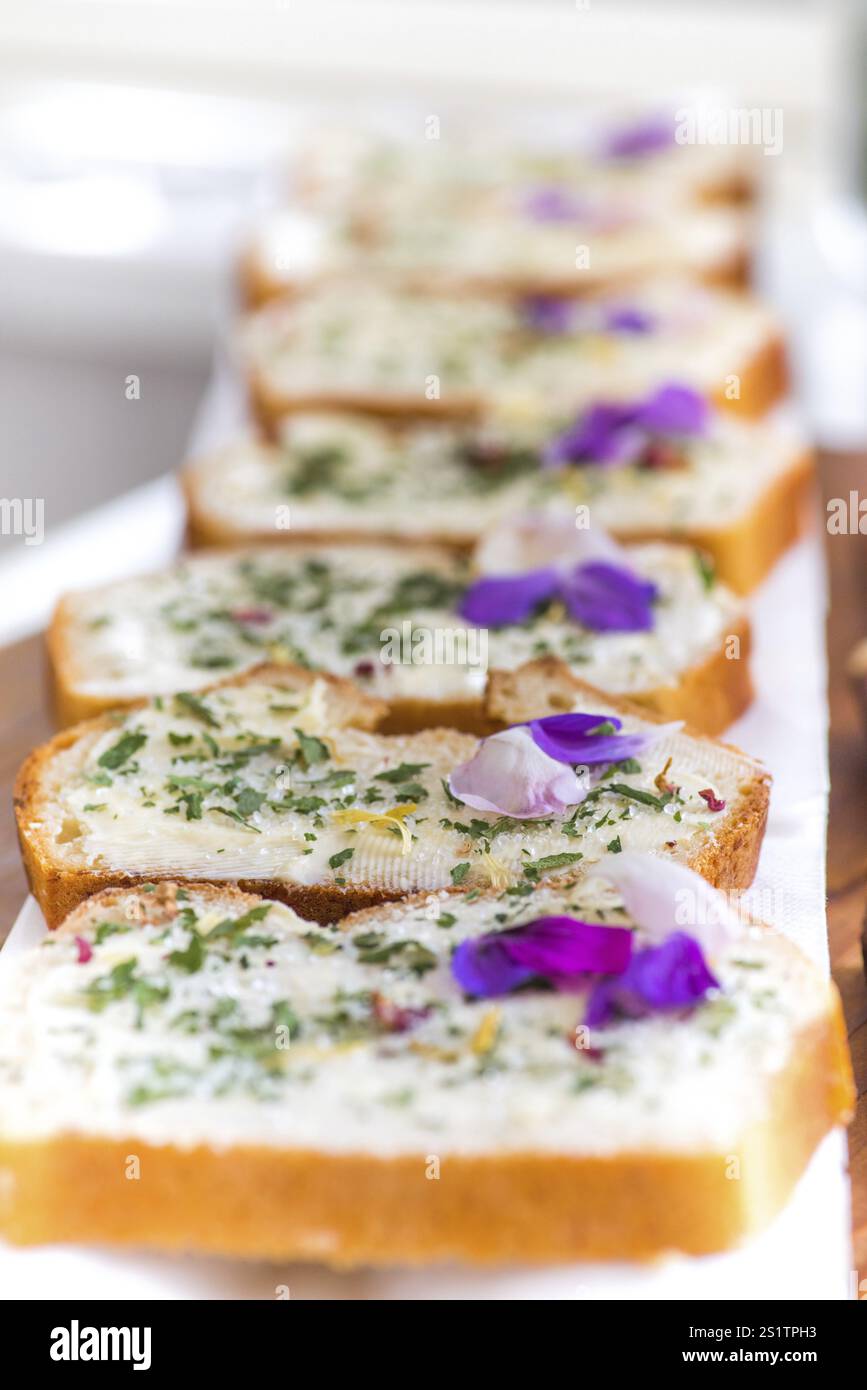 Delizioso pane al burro alle erbe con erbe e fiori del giardino estivo. Pane bianco con burro ed erbe aromatiche del giardino Foto Stock