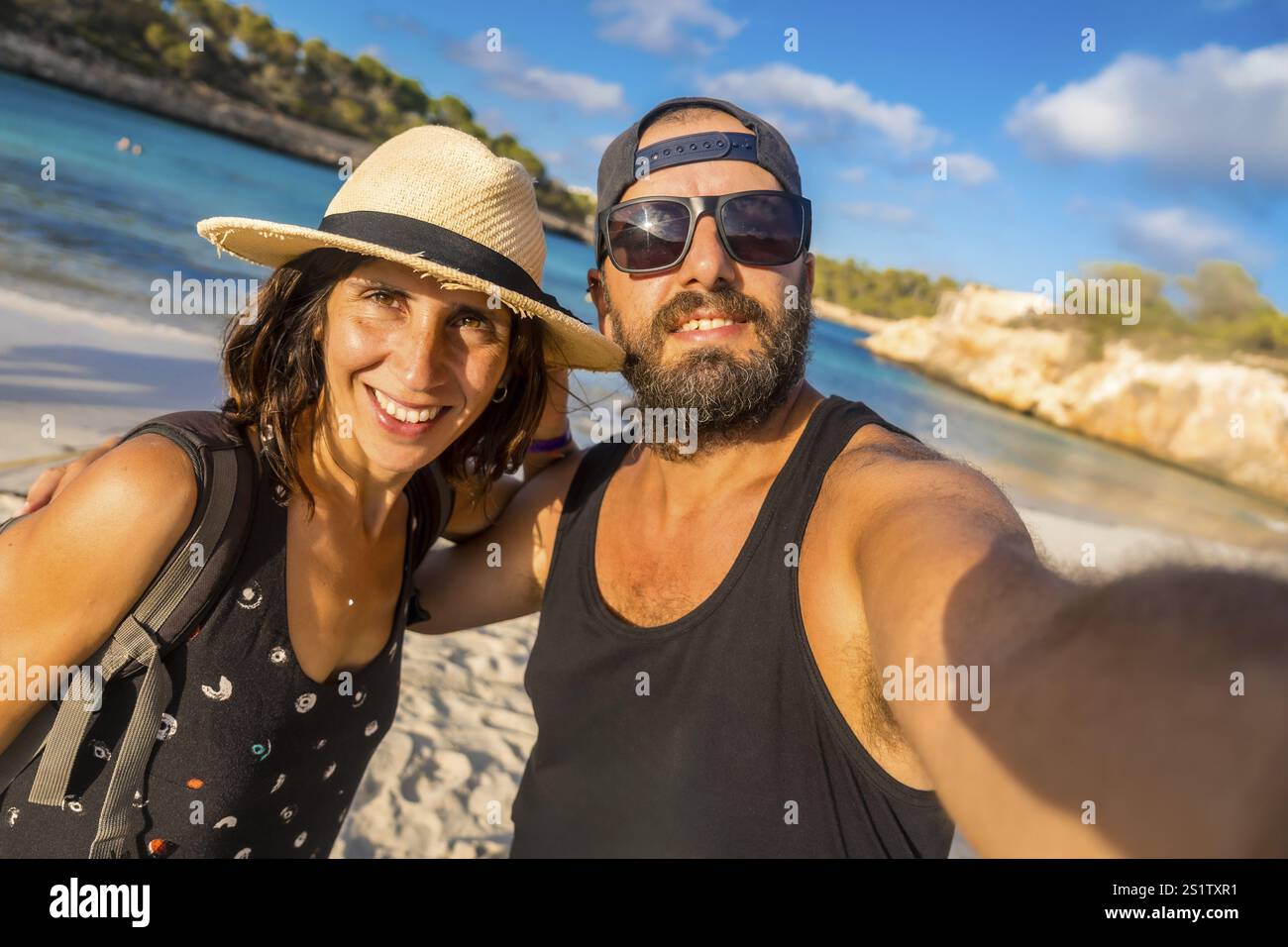 Un uomo e una donna stanno posando per una foto su una spiaggia. L'uomo indossa una canotta nera e occhiali da sole, mentre la donna indossa un cappello di paglia. Loro Foto Stock