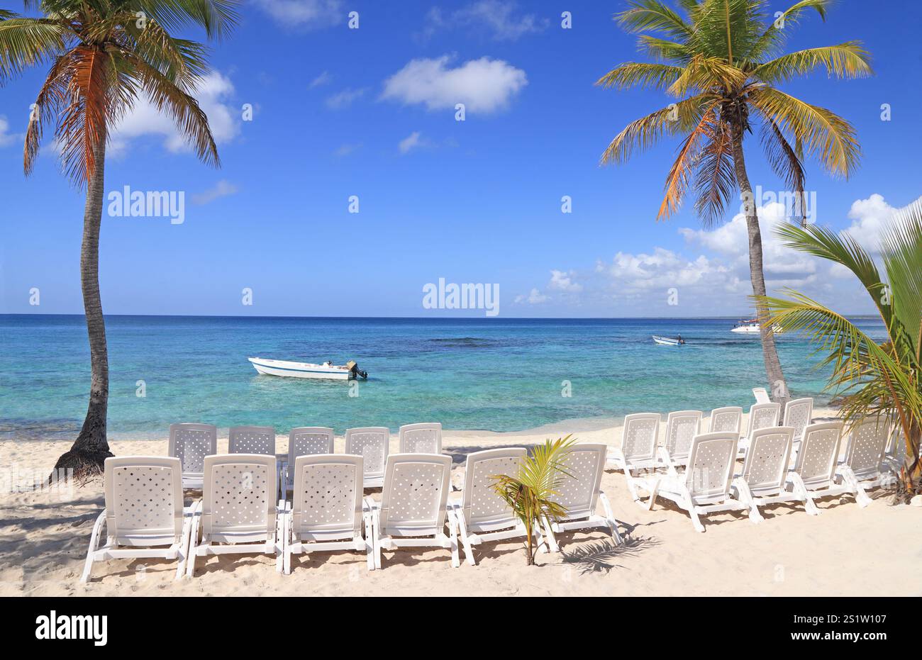 Bellissima spiaggia con sedie bianche e sabbia bianca in primo piano e cielo blu sullo sfondo dell'isola di Saona, Repubblica Dominicana Foto Stock