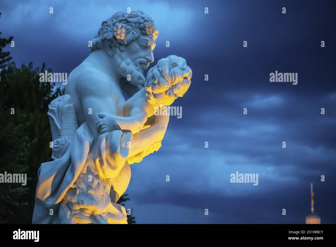 Statua in marmo di un uomo che tiene in braccio un bambino piccolo al castello di Karlsruhe, bellissimo illuminato la sera. Sculpure di un uomo forte che tiene una piccola c Foto Stock