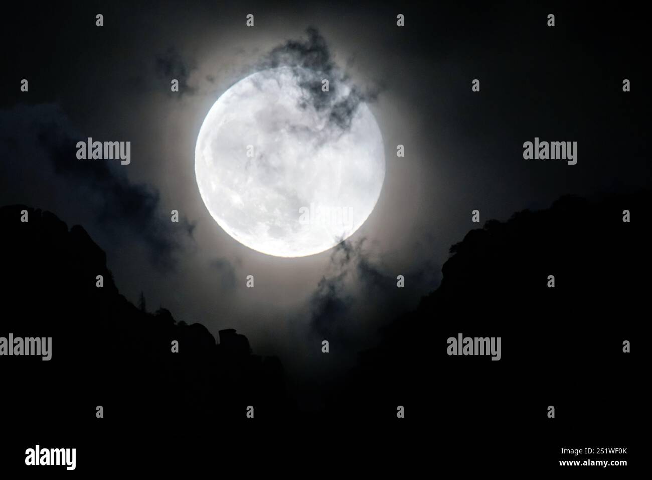 Luna piena che si innalza sulle montagne con nuvole discontinue Foto Stock