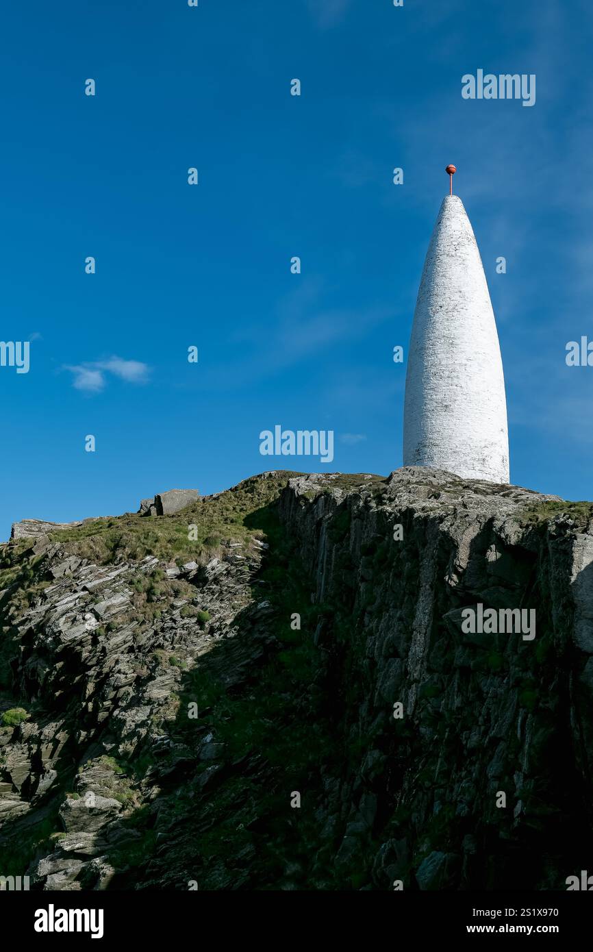 Situata in cima a una scogliera rocciosa, un'alta torre conica bianca si erge in modo prominente su uno sfondo blu brillante. Foto Stock