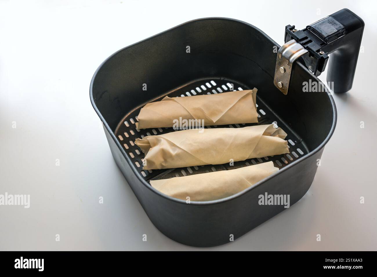 Rotoli di pasta fillo ripieni crudi o involtini primavera nel cestello di una friggitrice ad aria calda su un banco da cucina leggero, cottura sana con basso contenuto di grassi, copia Foto Stock