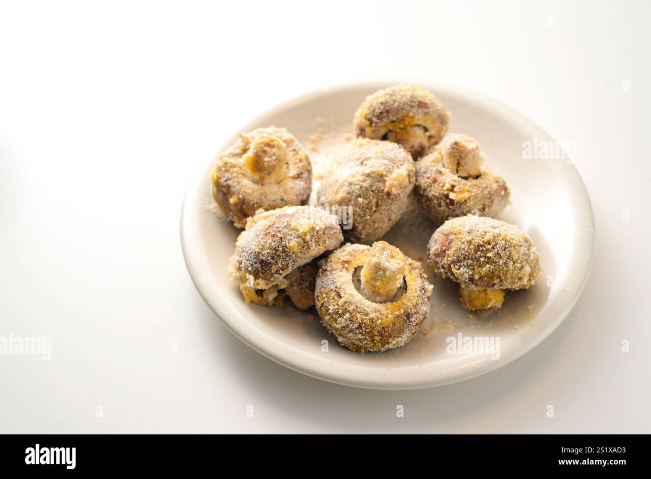 Funghi impanati su un piatto bianco, pronti per essere fritti in profondità o cotti nel forno, preparazione per uno spuntino di festa da verdure, spazio per copiare, f Foto Stock