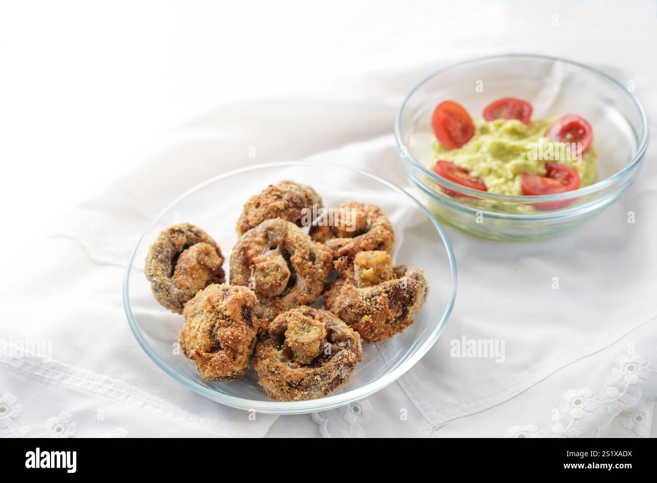 Funghi impanati cotti in una friggitrice ad aria calda e guacamole all'avocado immersi in ciotole di vetro su un tovagliolo bianco, spazio per le copie, messa a fuoco selezionata, profondità ridotta delle foto Foto Stock
