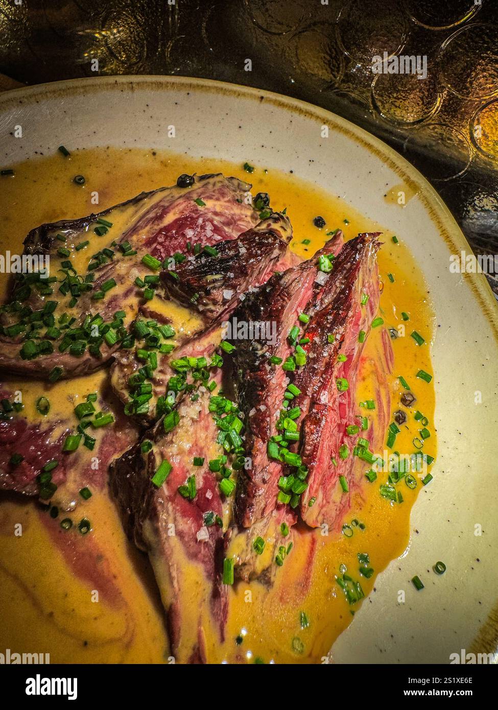Deliziosa bistecca di manzo a fette, appoggiata su un letto di salsa cremosa e guarnita con erba cipollina fresca, presentata su un piatto elegante, ottimo esempio di bistrono Foto Stock