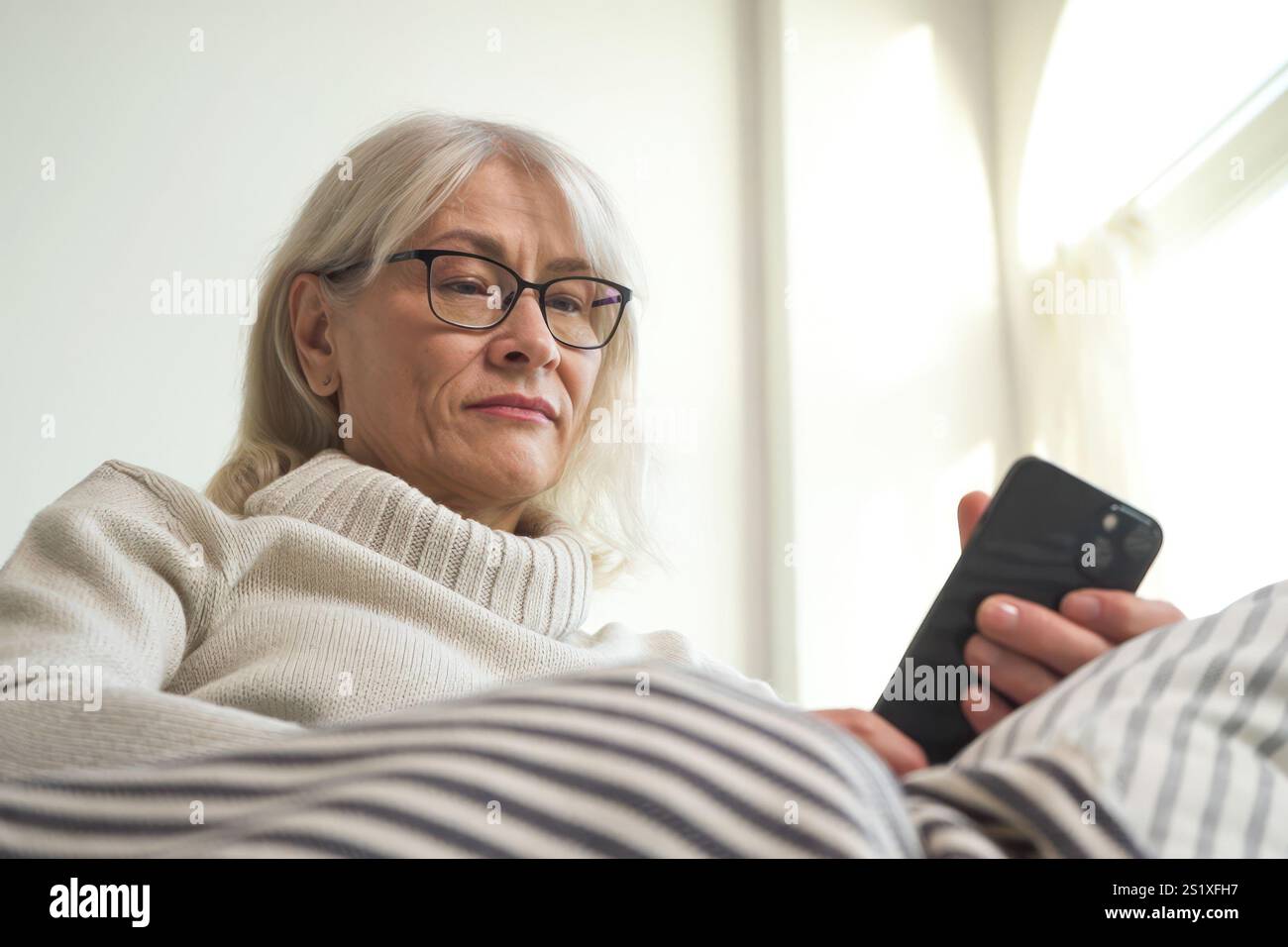 Donna anziana che si sente sospetta mentre controlla il suo smartphone Foto Stock