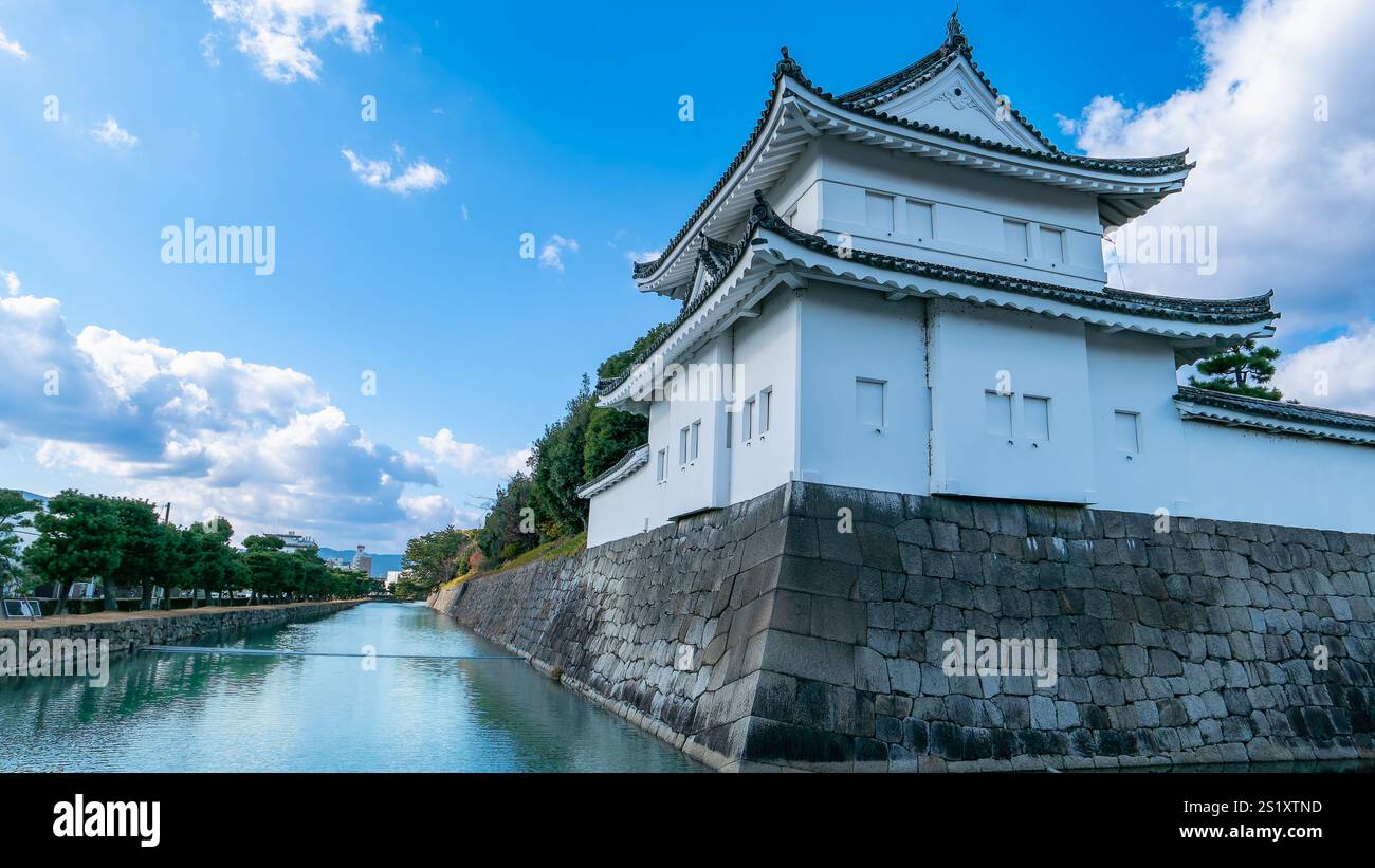 Un tranquillo corso d'acqua scorre dolcemente oltre le mura in pietra del Castello Nijo, riflettendo l'elegante facciata bianca del castello e l'intricata architettura. Kyoto, Giappone. Foto Stock