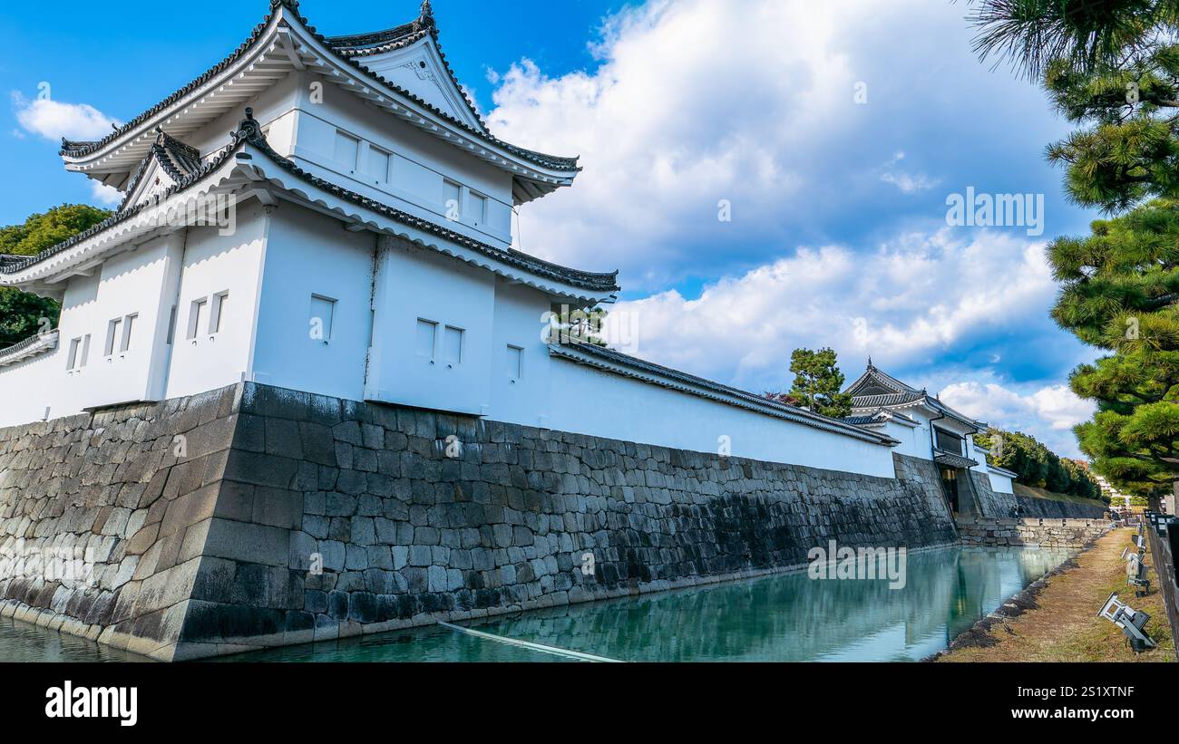 Un tranquillo corso d'acqua scorre dolcemente oltre le mura in pietra del Castello Nijo, riflettendo l'elegante facciata bianca del castello e l'intricata architettura. Kyoto, Giappone. Foto Stock