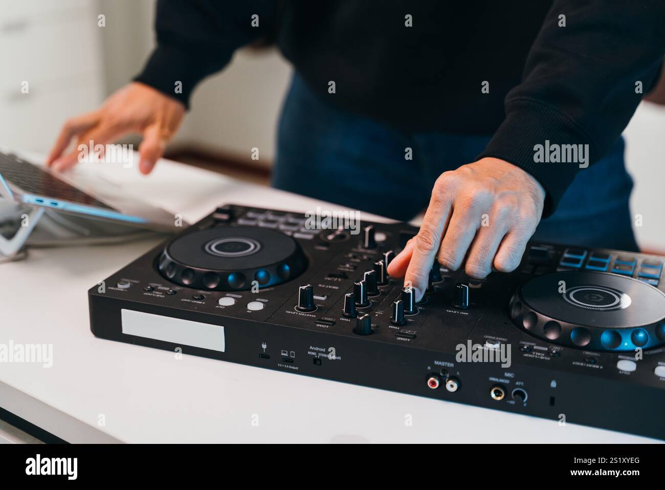 Primi piani di un DJ che mescola perfettamente brani su una console mixer minimalista in un elegante evento domestico. Foto Stock