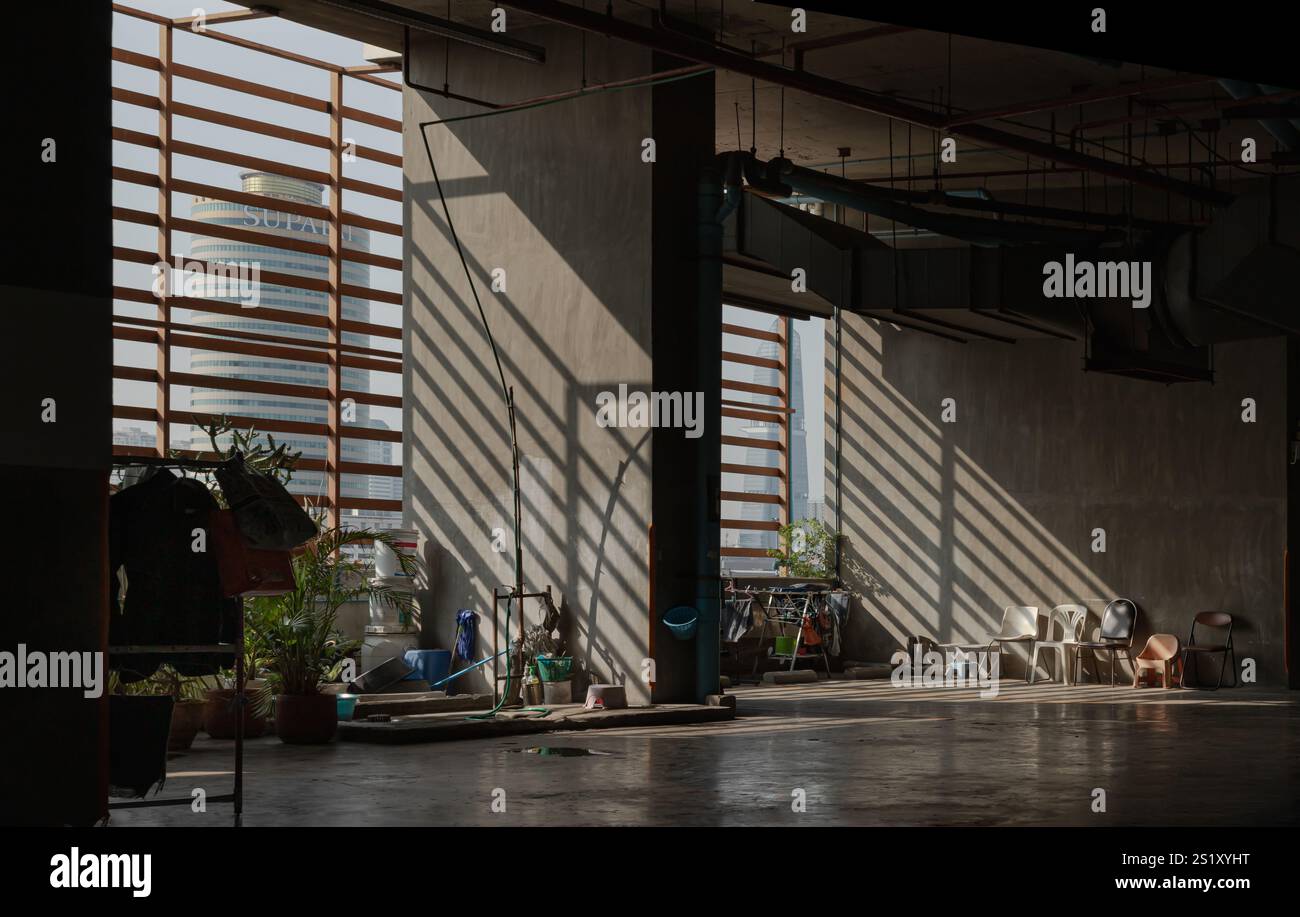 Bangkok, Tailandia 5 gennaio 2025 - la luce del sole del mattino splende attraverso le battute di legno fino all'area di lavaggio per cameriere e una varietà di sedie vicino alle pareti di cemento Foto Stock
