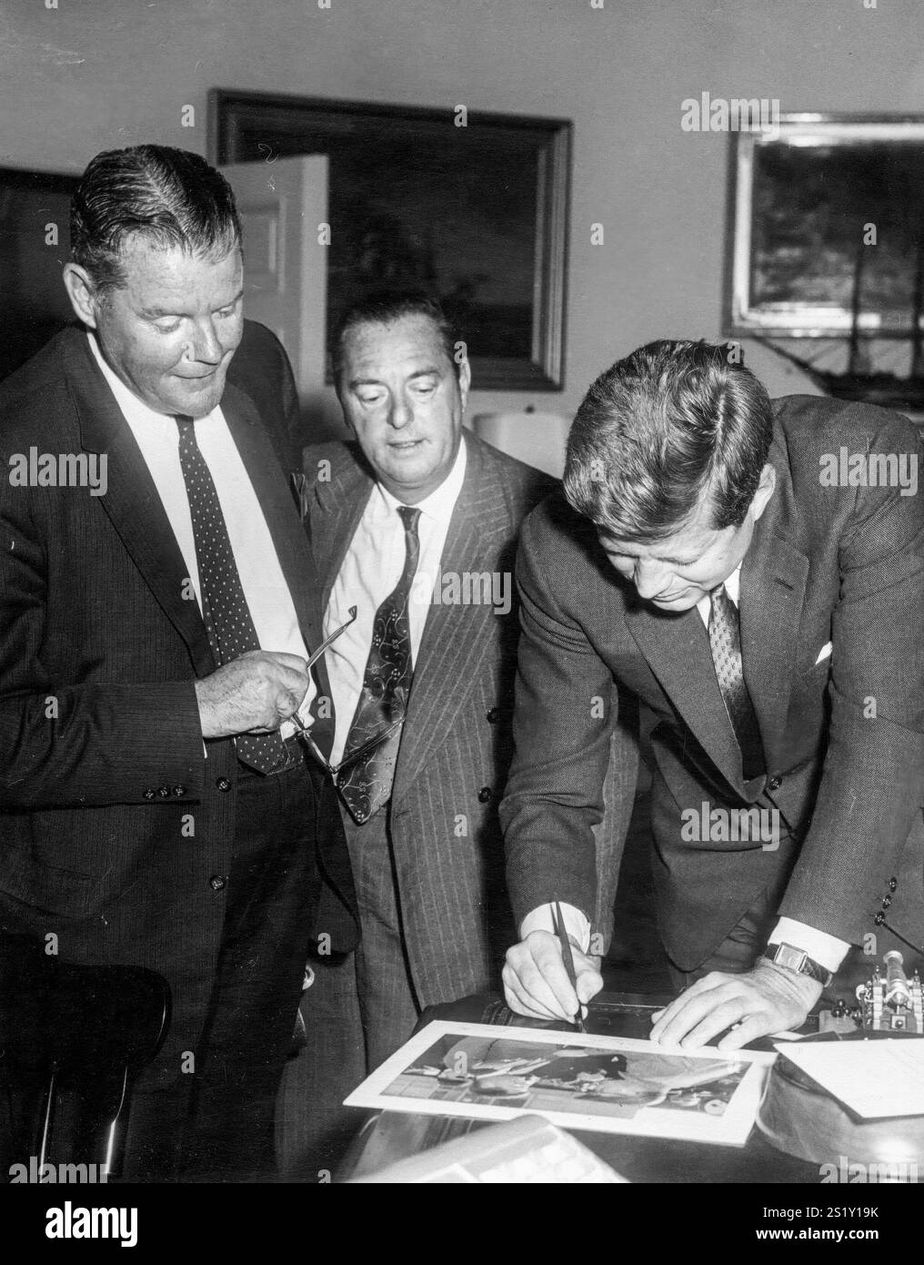 11 aprile 1961 il presidente John F. Kennedy firma una fotografia per uno dei vincitori del 18 ° concorso annuale White House News Photographers Association nell'Ufficio ovale, Casa Bianca, Washington, D.C. i vincitori includono: James K. W. Atherton; Wallace W. McNamee; Frank Cancellare; Wellner C. Streets; Thomas Shields; Elwood Baker e Robert F. Sisson. Foto Stock