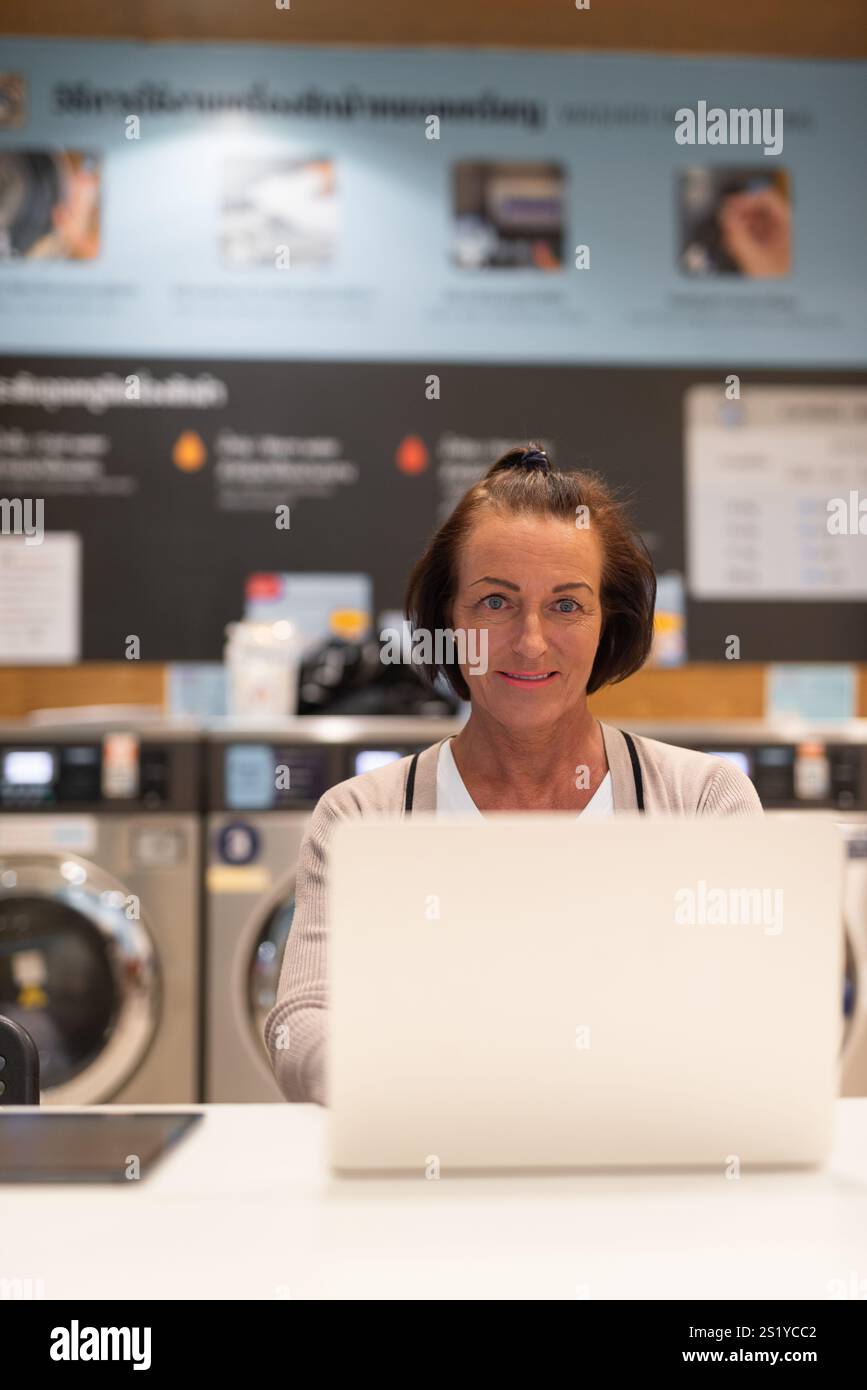 Donna che lavora su un computer in un negozio di lavanderia Foto Stock