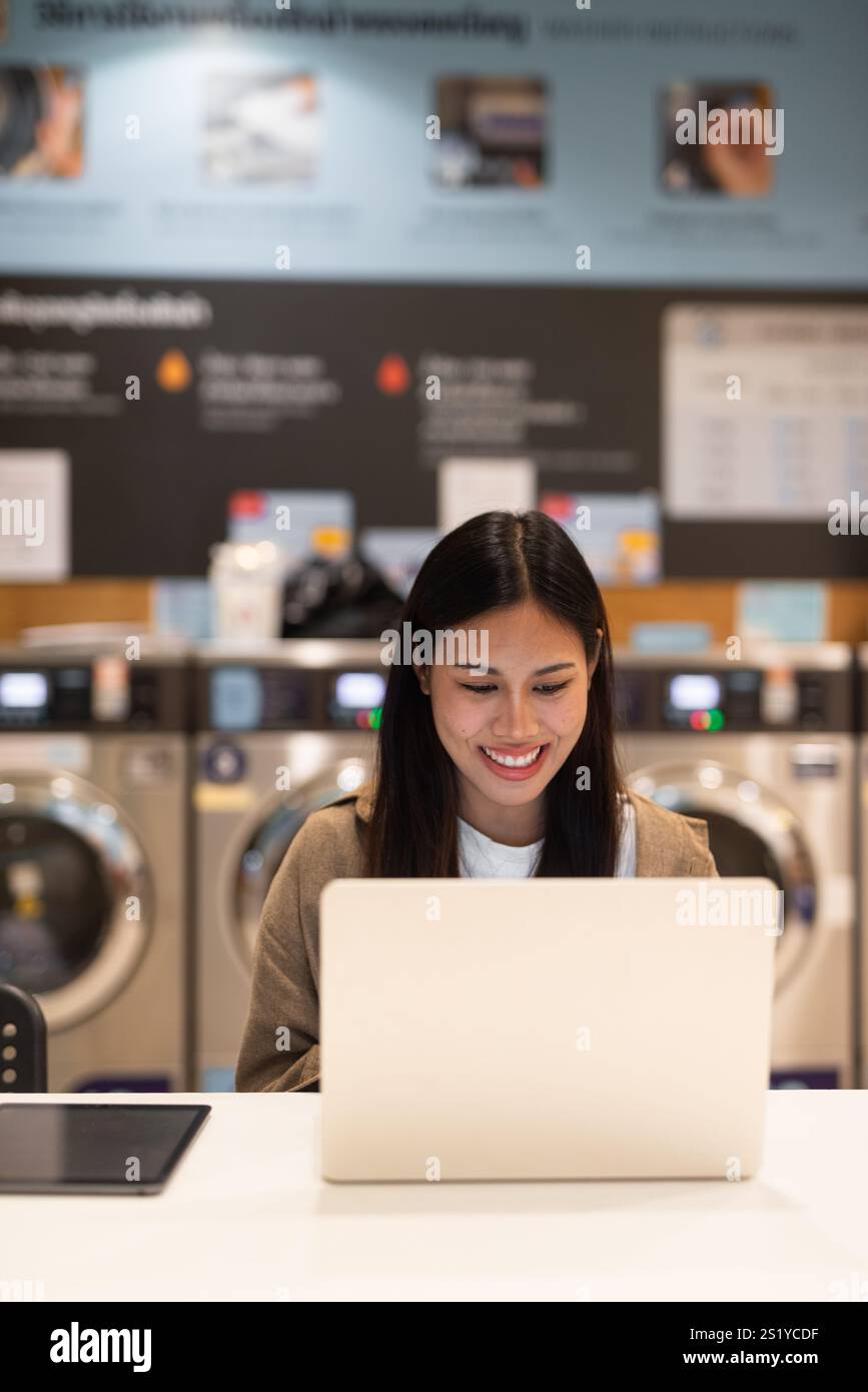 Donna che lavora su un notebook in un negozio di lavanderia Foto Stock