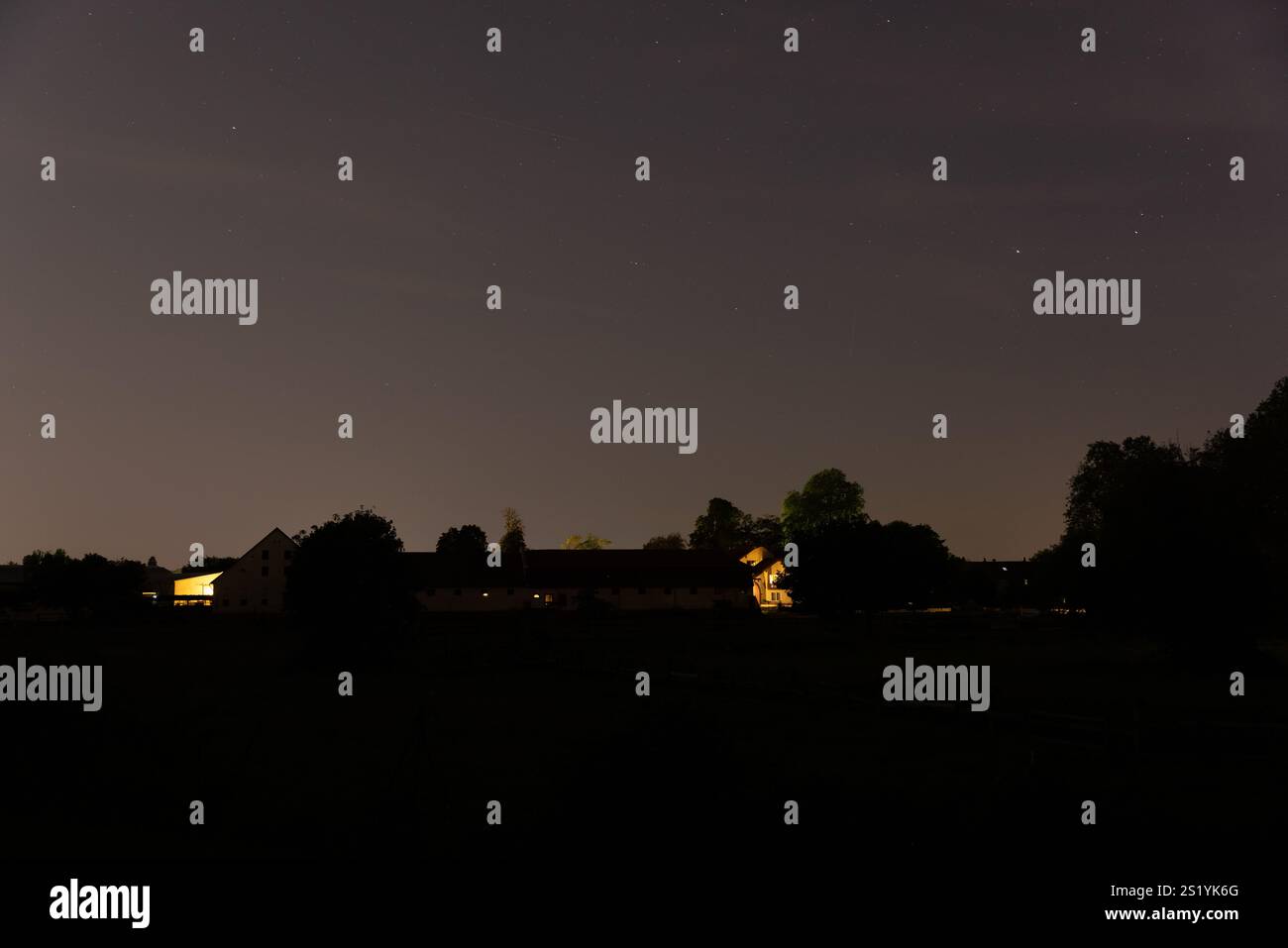 Una tranquilla scena rurale di notte con fattorie delicatamente illuminate circondate da alberi sotto un cielo stellato. Foto Stock